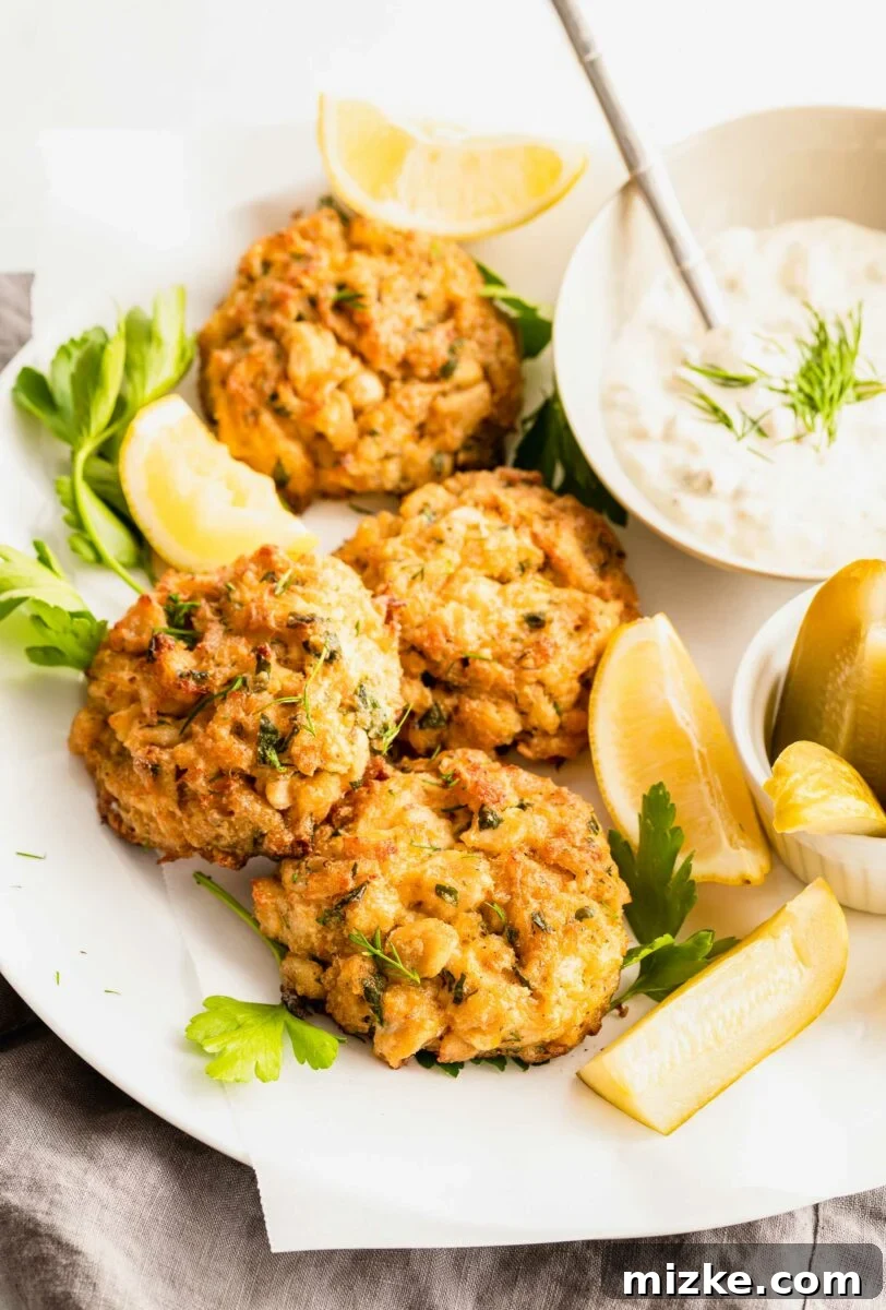 Ultimate Crab Cake Sandwiches 4 A delectable trio: golden-brown crab cakes, crisp pickle spears, and a generous dollop of creamy tartar sauce, perfectly arranged for a classic seafood meal.