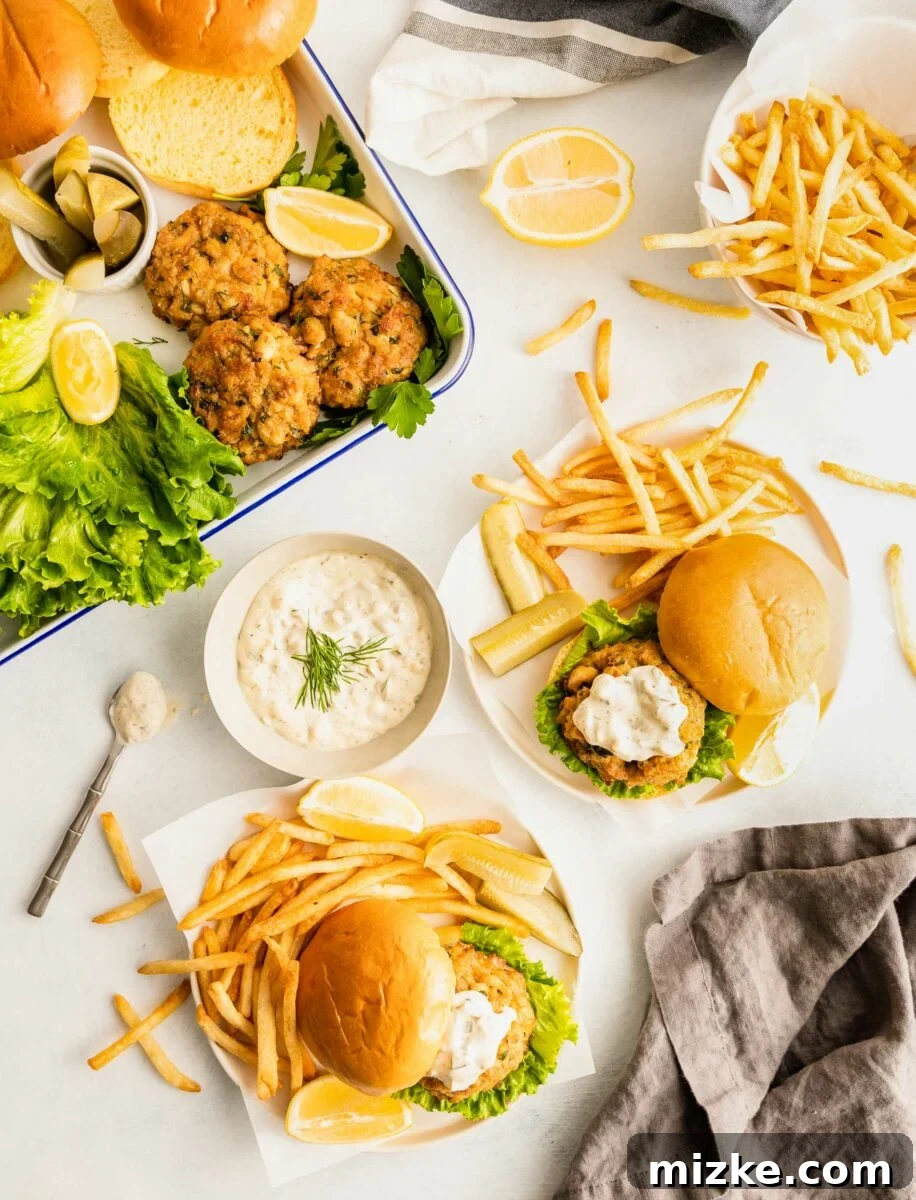 Ultimate Crab Cake Sandwiches 5 Two enticing plates, each holding a perfectly assembled crab cake sandwich nestled alongside a generous serving of golden, crispy French fries, promising a fulfilling and classic meal.