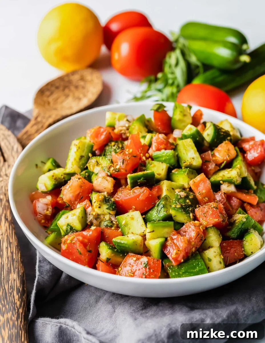 Mediterranean Za'atar Cucumber Tomato Salad 3 Freshly cut tomatoes and cucumbers, ready for a Za'atar salad, being tossed in a bowl with wooden servers next to whole, uncut vegetables on a rustic surface.