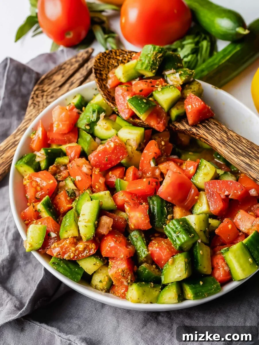 Mediterranean Za'atar Cucumber Tomato Salad 5 A large wooden spoon is serving a portion of the fresh and colorful Za'atar cucumber tomato salad from a white bowl, ready to be enjoyed.