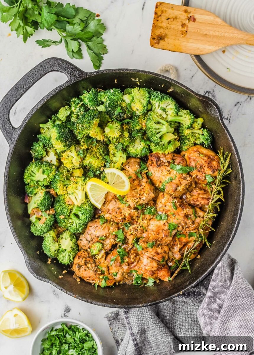 A lemon is twisted in the middle of a broccoli and chicken skillet, garnished with fresh herbs.