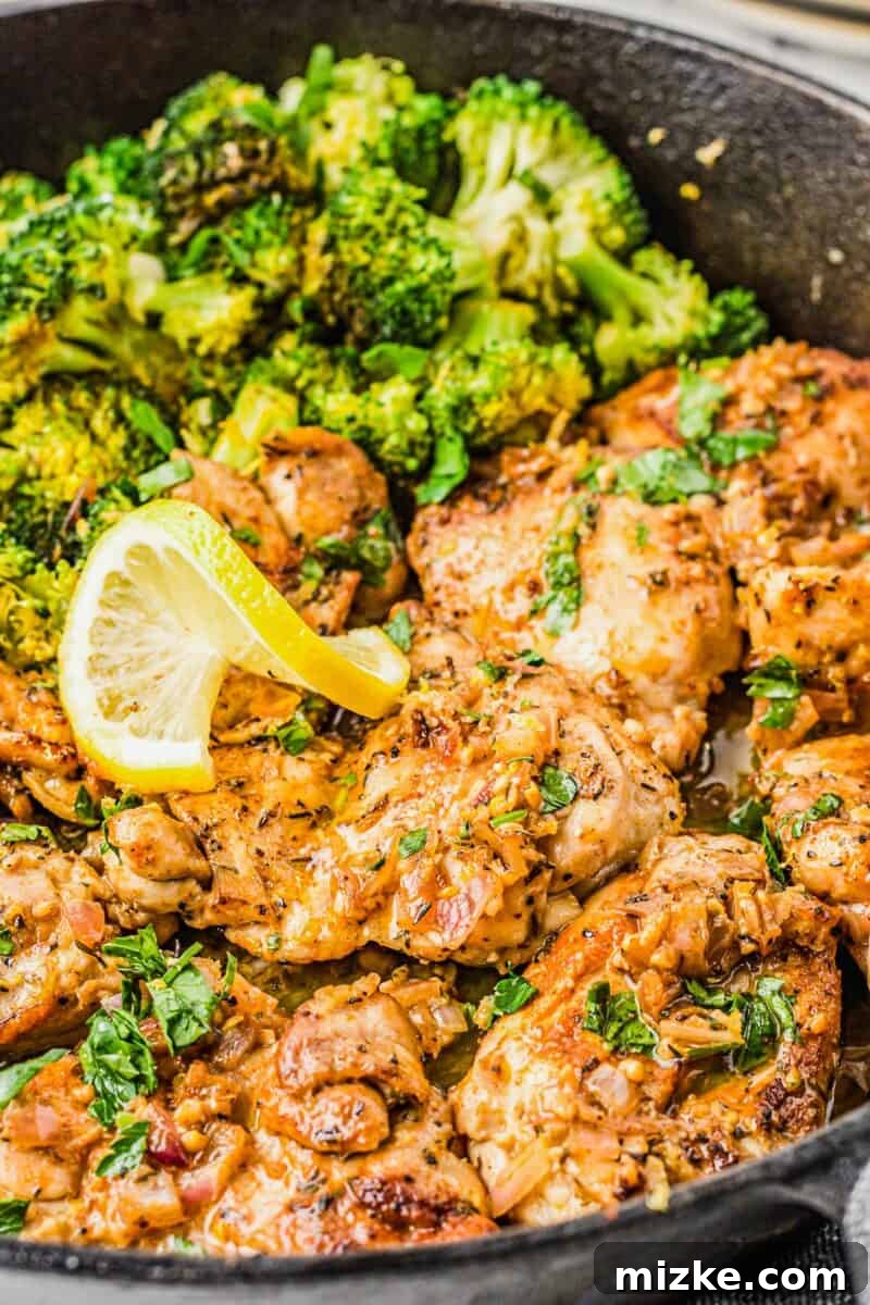 Fully cooked lemon garlic chicken thighs are arranged in a skillet next to steamed broccoli florets.