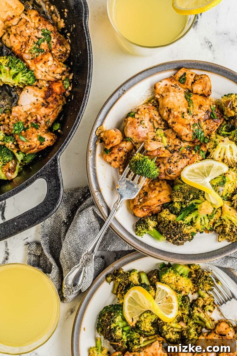 Two white plates with generous servings of lemon garlic chicken and broccoli are placed next to the skillet on a wooden table.