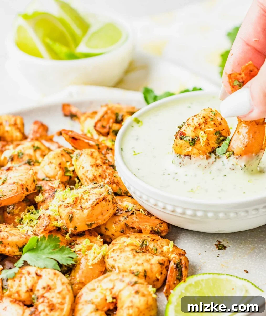 A succulent, golden-brown air-fried shrimp is being dipped into a small bowl of creamy green cilantro lime dressing, illustrating the perfect serving suggestion.