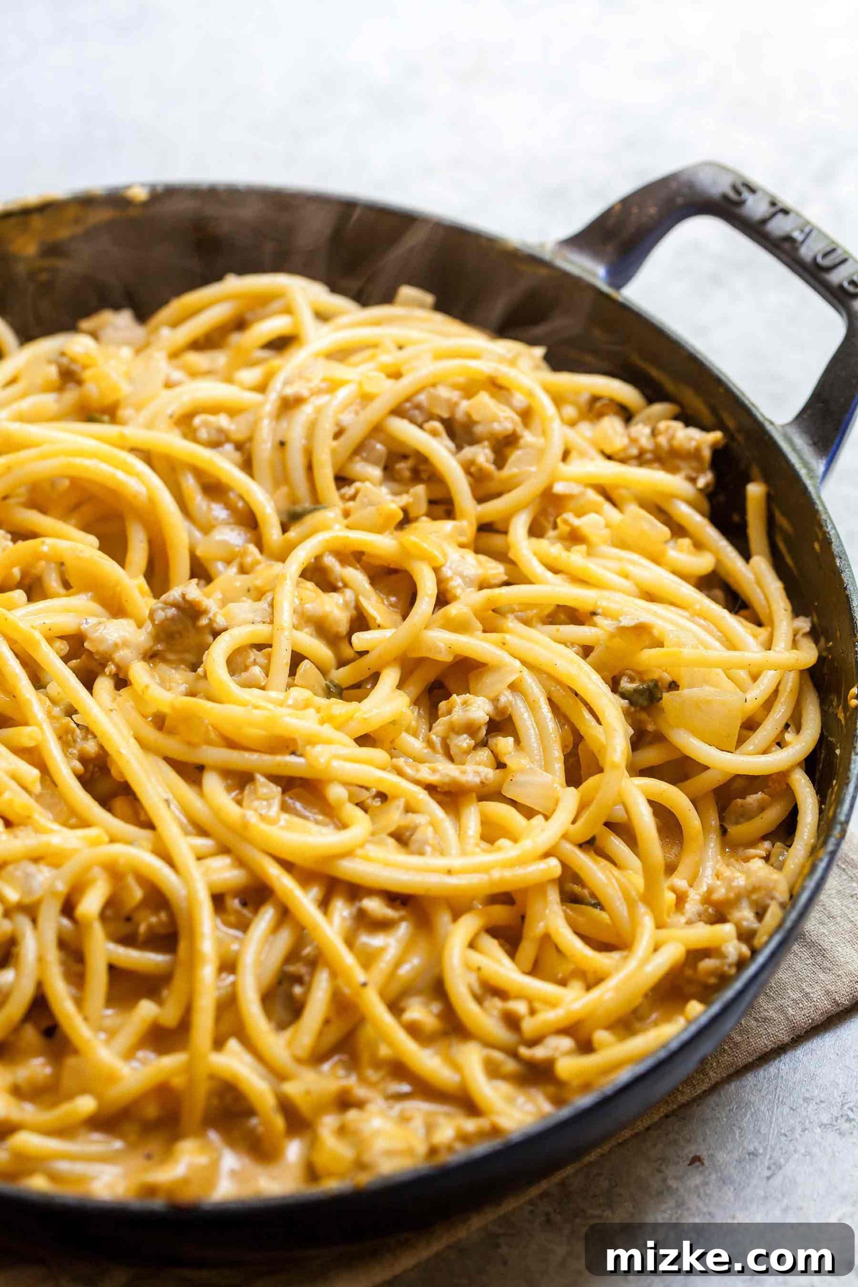Autumn Spiced Pumpkin Pasta with Turkey Sausage 4 Close-up overhead shot of creamy pumpkin pasta with turkey sausage in a Staub skillet, garnished with fresh sage