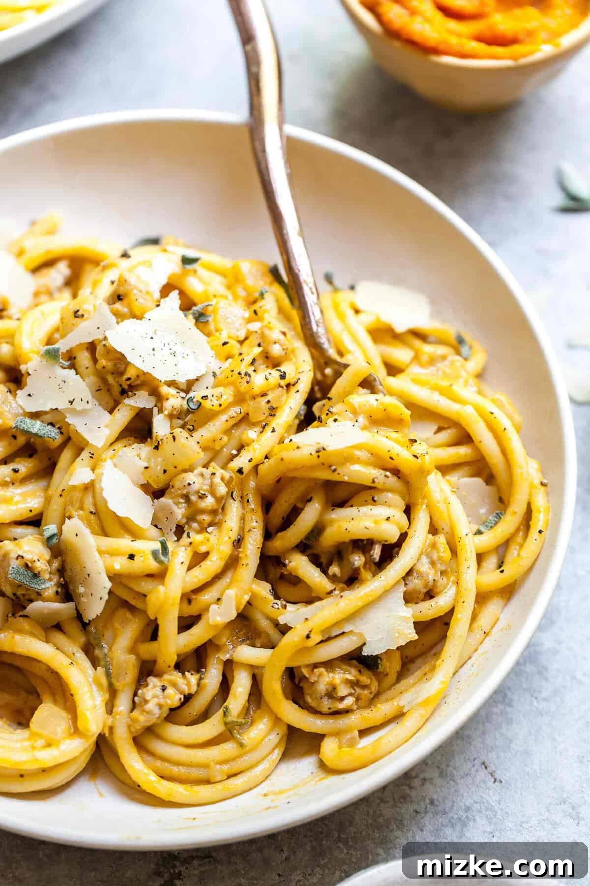 Autumn Spiced Pumpkin Pasta with Turkey Sausage 5 Close-up photo of creamy pumpkin pasta with turkey sausage in white bowl, topped with freshly cracked black pepper and a sprig of sage