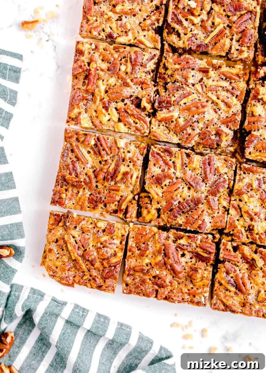 Golden Pecan Pie Squares 2 Overhead shot of freshly baked pecan pie bars cut into uniform squares, arranged beautifully on a pristine white background, accompanied by a charming blue and white striped linen towel.