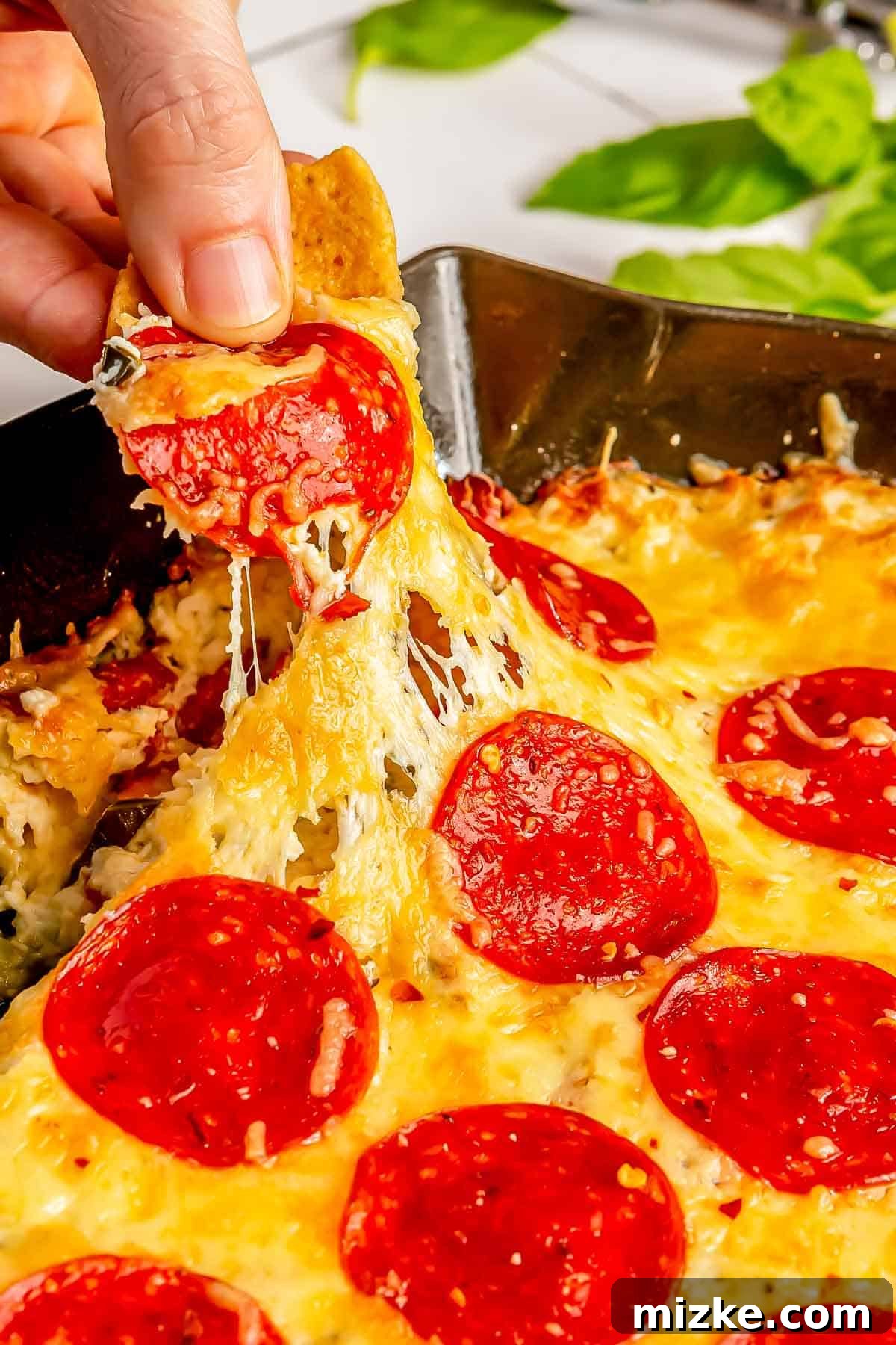 Cheesy Pepperoni Pizza Bake 3 A corn tortilla scoop actively being dipped into a hot, cheesy pepperoni pizza dip, showcasing its gooey texture