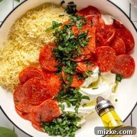 Ingredients for pizza dip being mixed in a black rimmed white bowl, with olive oil actively being poured in