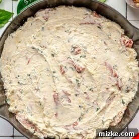Pizza dip mixture spread evenly in a cast iron skillet, ready for toppings