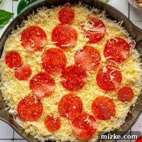 Pepperoni pizza dip topped generously with fresh mozzarella cheese and whole pepperoni slices, ready for baking
