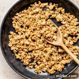 Crumbled breakfast sausage browning in a skillet with a wooden spoon, releasing savory aromas.