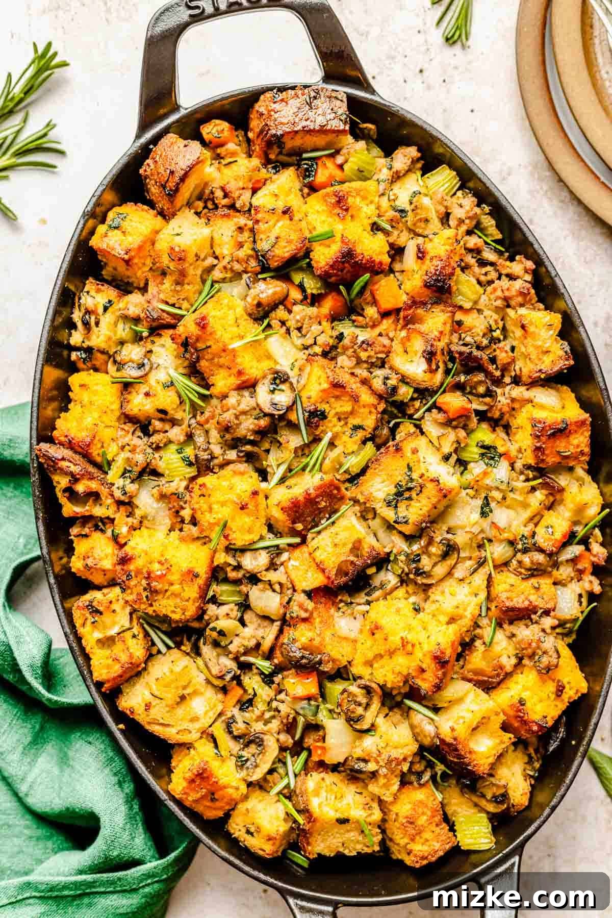 A close-up of cornbread and sausage stuffing in a black cast iron baking dish, resting on a green linen towel, highlighting its crispy top and savory texture.