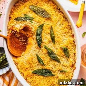Baked savory sweet potato casserole with a golden breadcrumb topping and sage leaves, served in a white dish with a wooden spoon and a portion plated nearby.