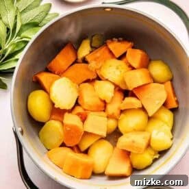 Rustic Savory Sweet Potato Bake 5 A pot filled with chunks of cooked sweet potatoes and potatoes, surrounded by fresh sage leaves, a dish of salt and pepper, and a bowl of breadcrumbs.