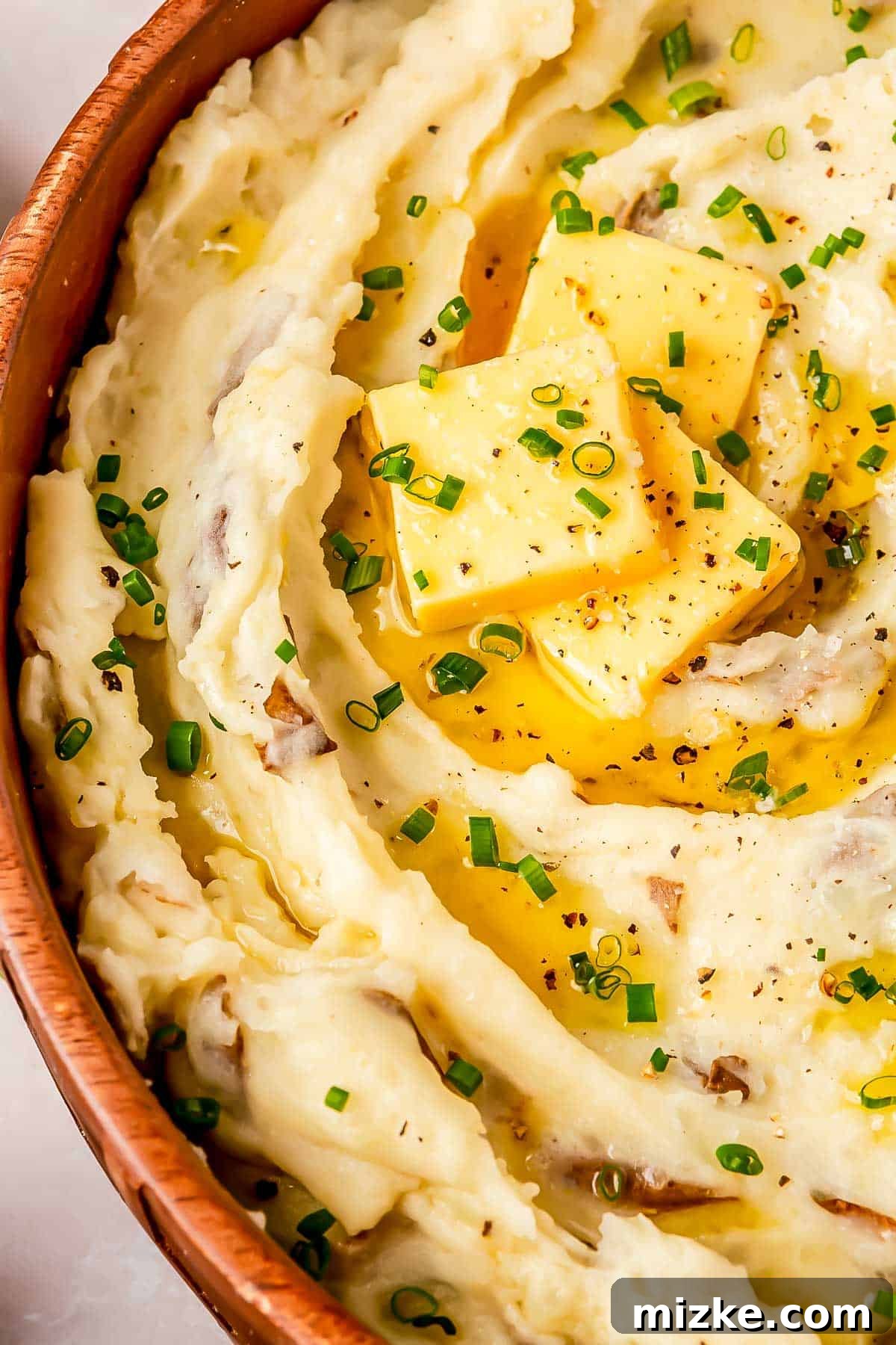 Heavenly Garlic Mashed Potatoes 4 A close-up view of the rich, creamy texture of garlic mashed potatoes, with three distinct pats of butter slowly melting and pooling in the inviting ridges, ready for serving.