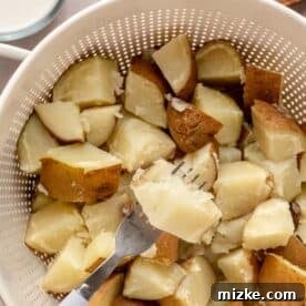 Heavenly Garlic Mashed Potatoes 6 Cooked russet potato chunks being drained in a colander, with a fork demonstrating how easily one piece can be pierced.