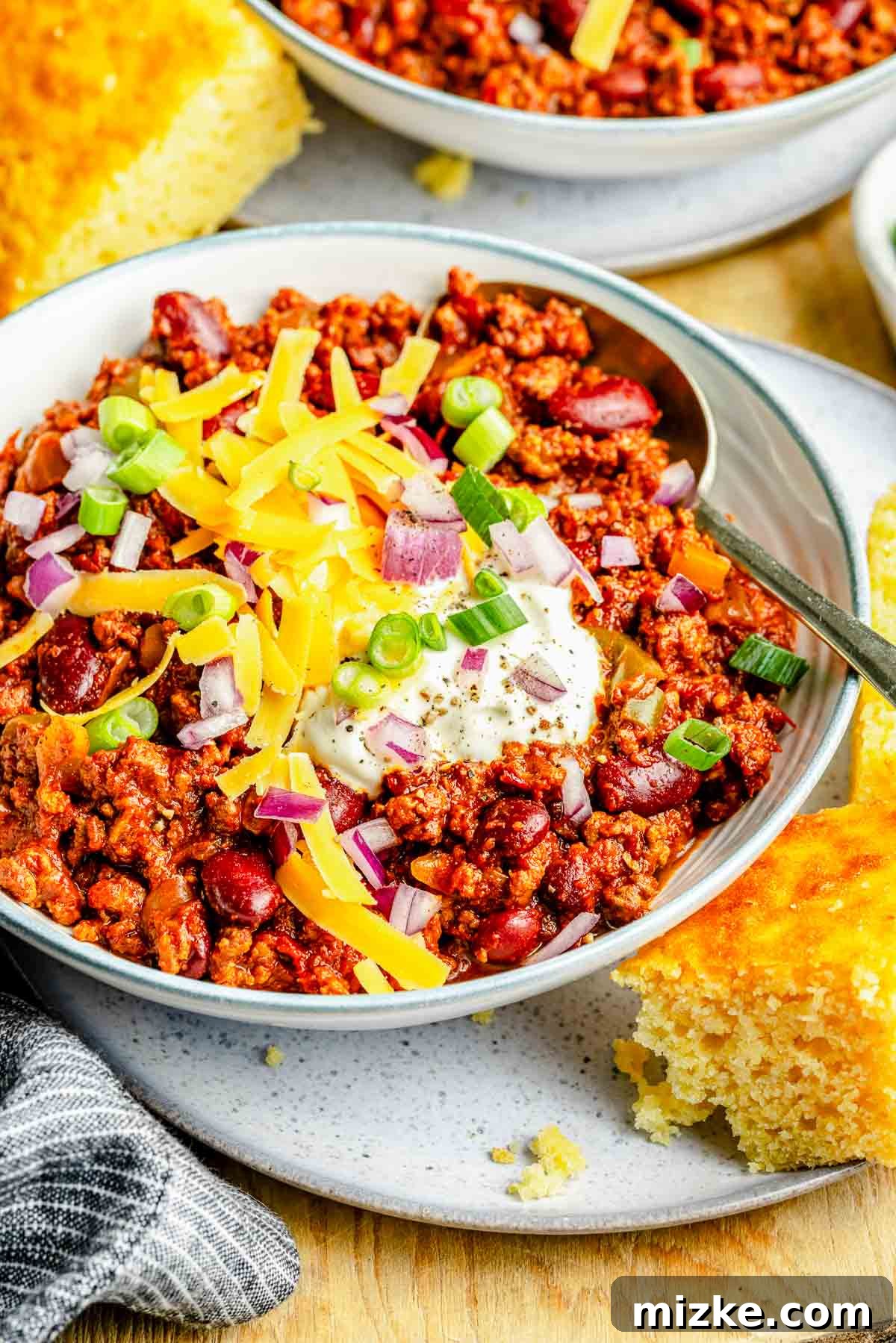 Hearty slow cooker chili with multiple meats, beans, and spices, perfect for a cozy meal. A steaming bowl of slow cooker chili, generously loaded with fresh toppings like shredded cheese, diced red onions, and a dollop of sour cream, ready to be enjoyed.