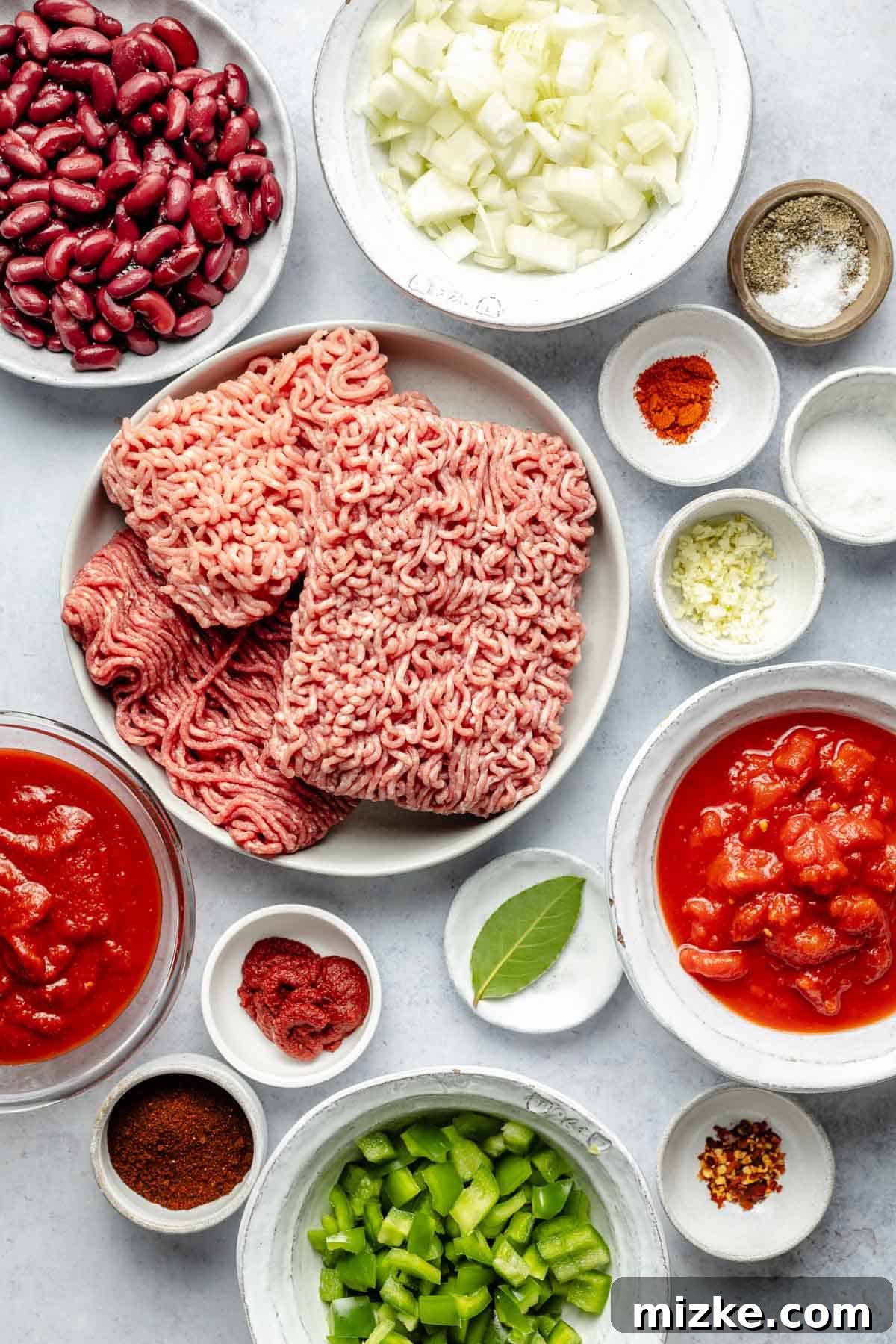 Essential ingredients for a rich and flavorful slow cooker chili with multiple meats and spices. All the fresh and canned ingredients neatly arranged for making slow cooker chili, including ground meat, onions, bell peppers, tomatoes, and various spices.