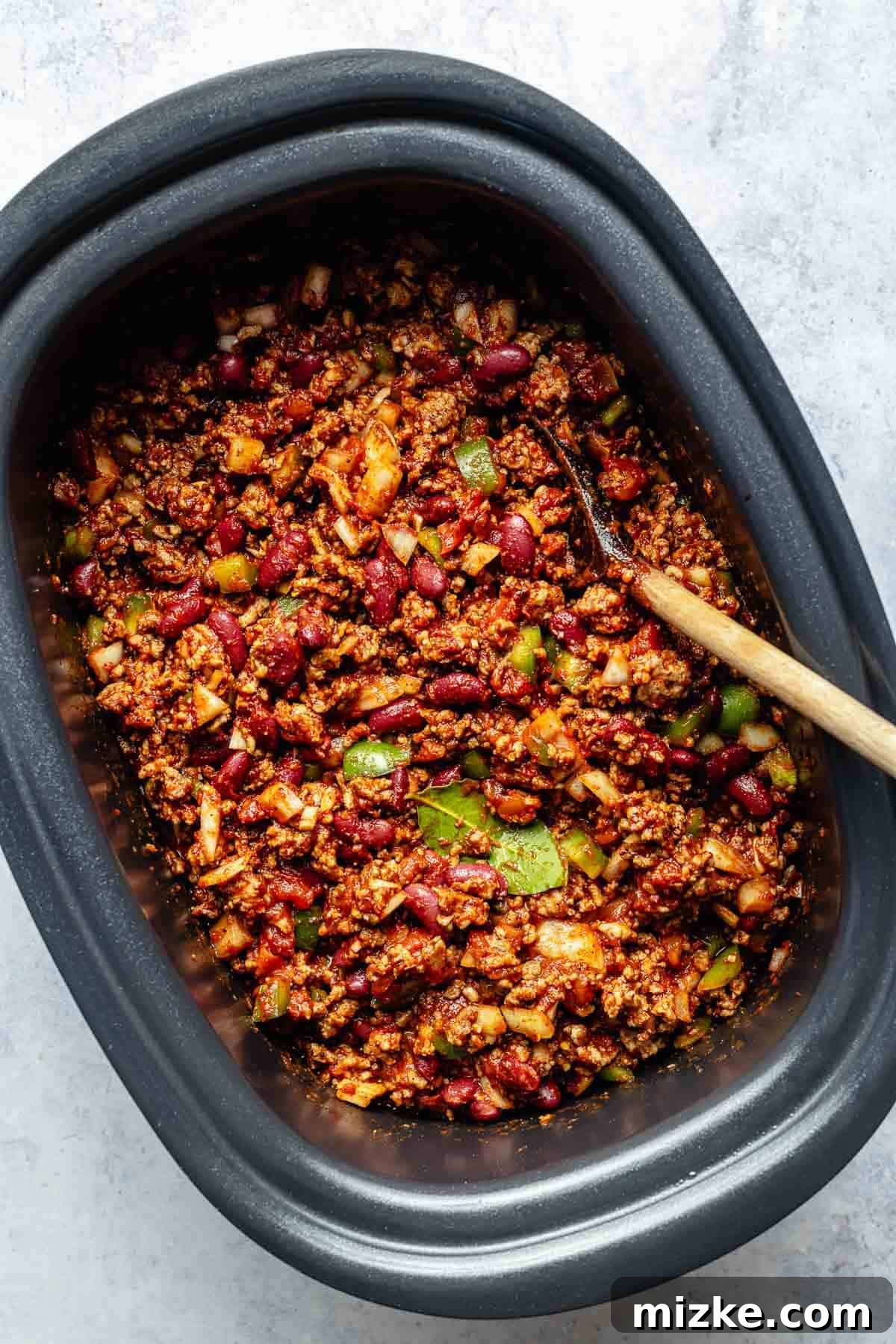 All the delicious ingredients for slow cooker chili, mixed and ready for slow cooking. An overhead view of the slow cooker filled with all the chili ingredients, including browned meat, beans, vegetables, and tomato base, before cooking.