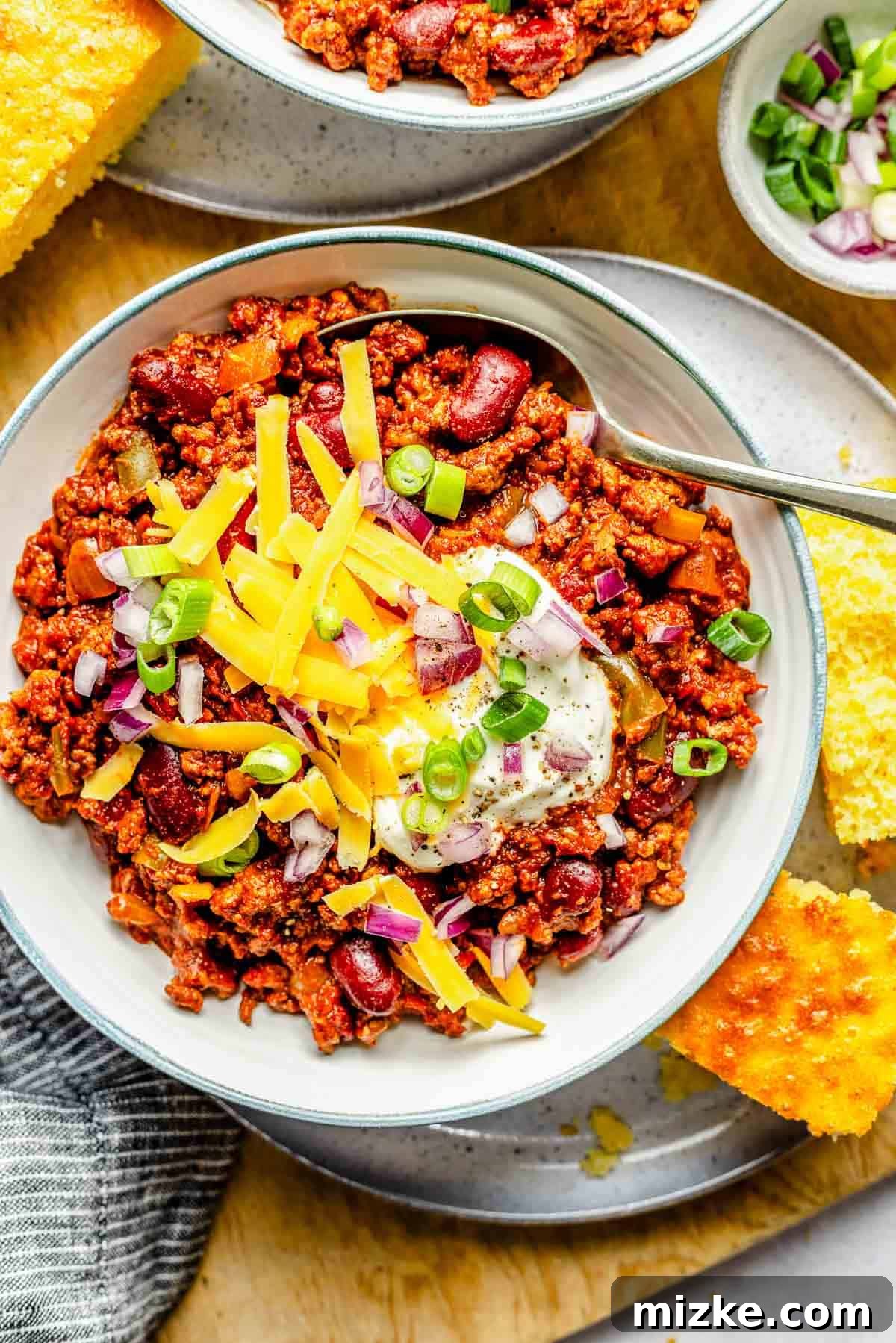 A perfectly crafted bowl of slow cooker chili with all the classic toppings. An overhead shot of a single bowl of slow cooker chili, artfully topped with vibrant shredded cheddar cheese, fresh green onions, and a dollop of sour cream.