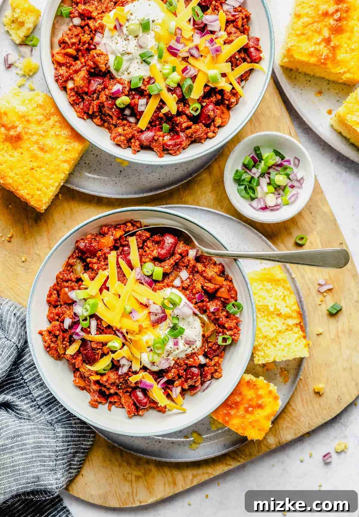 Two inviting bowls of slow cooker chili, beautifully presented and ready to be savored. A delightful overhead image showcasing two bowls of slow cooker chili, each generously topped with various garnishes, set on a rustic wooden surface.