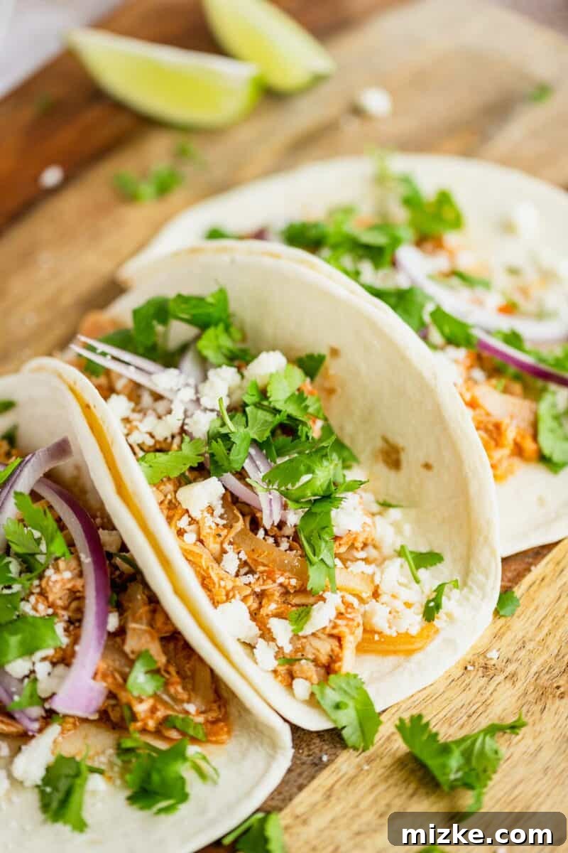 Easy Slow Cooker Chicken Tinga Tacos 2 Delicious chicken tinga tacos arranged on a rustic wooden surface, ready to be served.