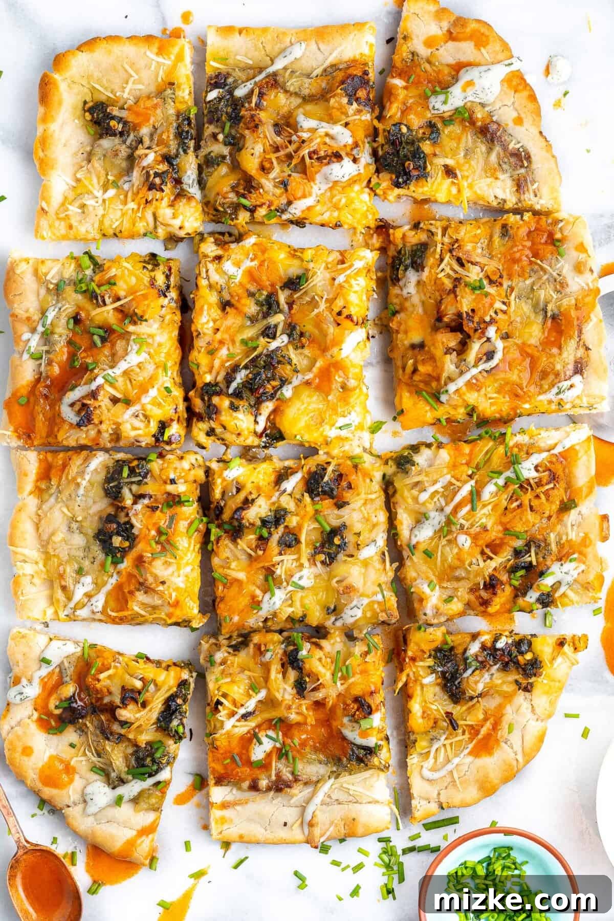 Bold Buffalo Cauliflower Pizza 2 A vibrant Buffalo Cauliflower Pizza, generously drizzled with creamy ranch sauce and buffalo sauce, cut into square pieces.