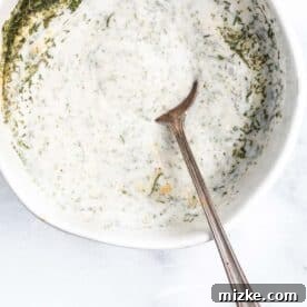 A metal spoon mixing the creamy vegan ranch sauce ingredients in a white bowl.