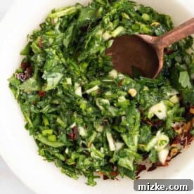 A wooden spoon mixing a blend of fresh herbs, minced garlic, and red pepper flakes in a white bowl.
