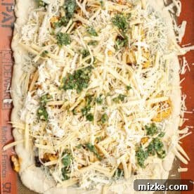 An assembled Buffalo Cauliflower Pizza, with all toppings and cheese spread over the dough on a silicone baking mat, ready for baking.