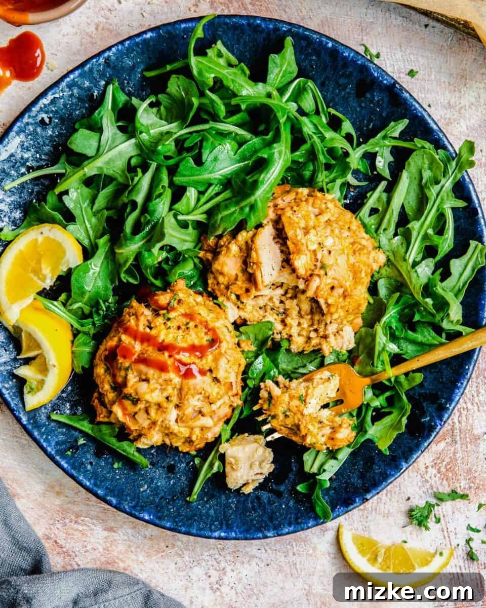 Golden Tuna Patties 2 Two golden-brown tuna cakes are beautifully arranged on a bed of fresh arugula on a blue plate, garnished with a lemon wedge.