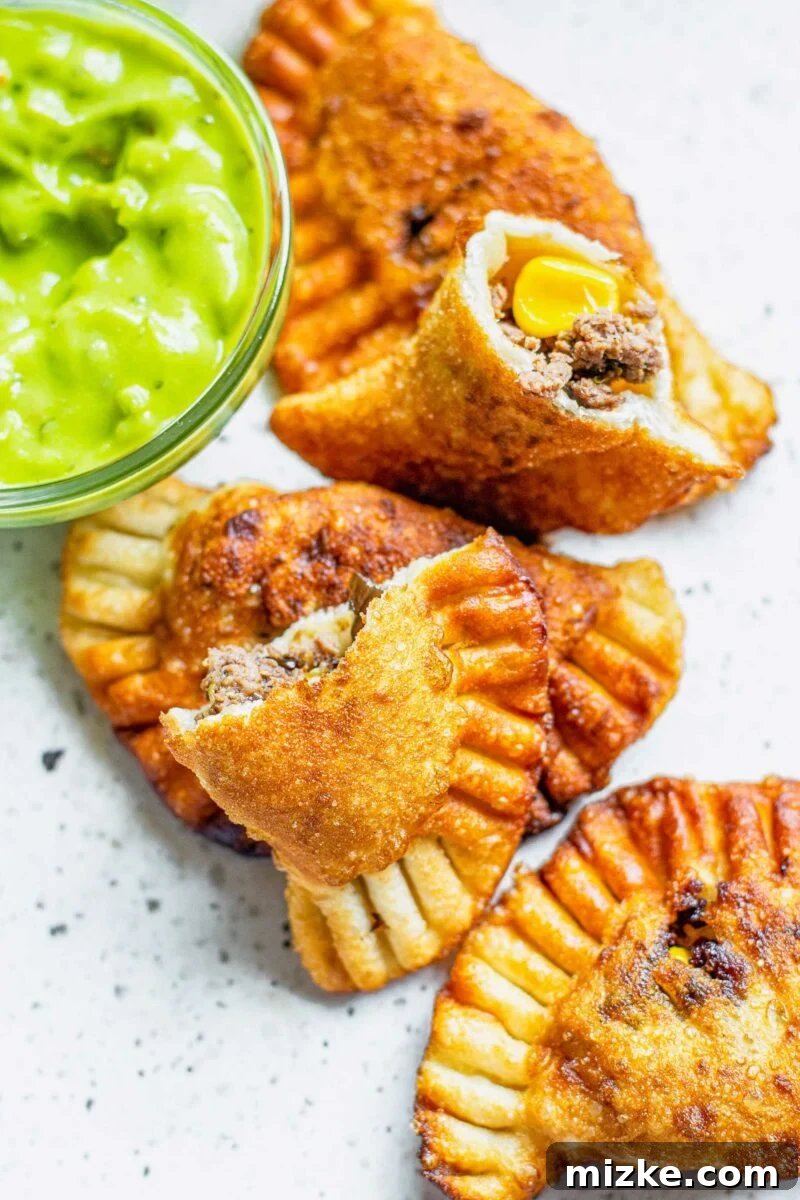 One beef empanada has been perfectly split in half, showcasing its rich, savory filling, placed alongside several whole, golden-brown empanadas on a white surface.