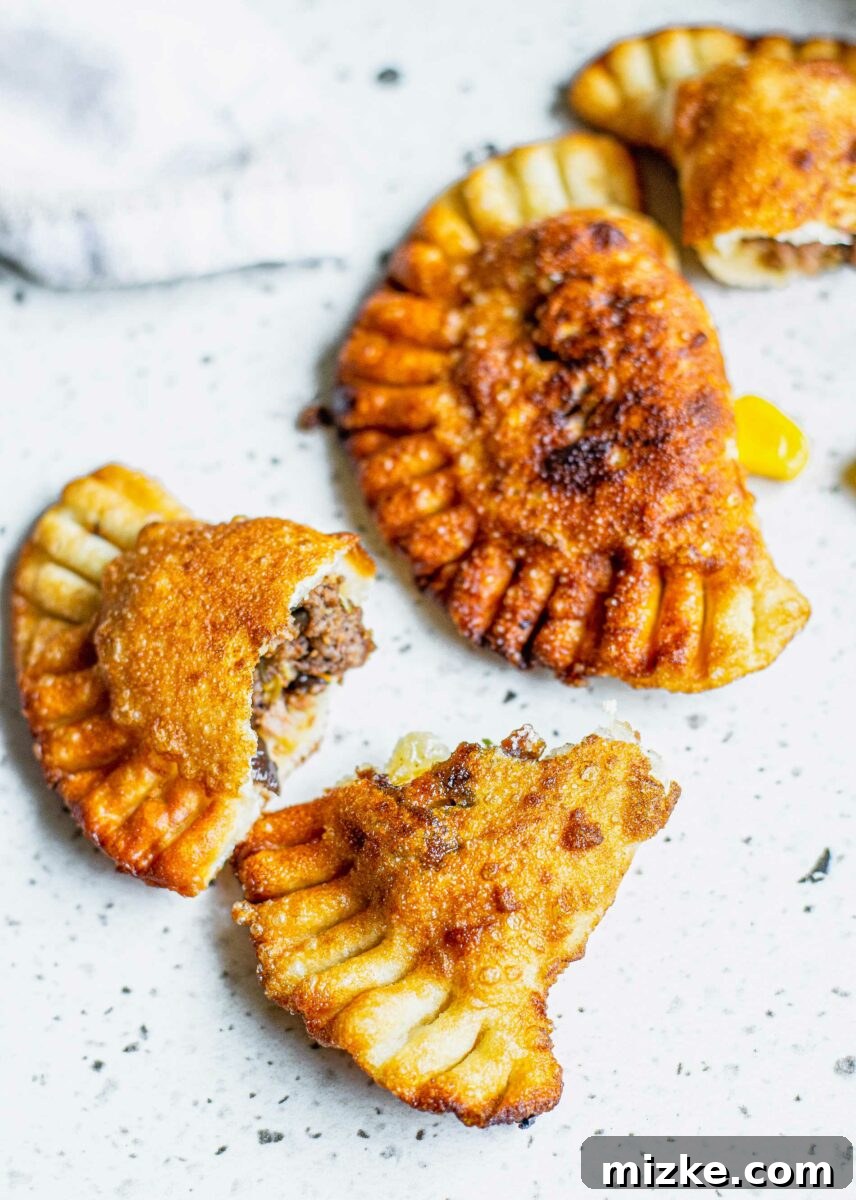 A single, perfectly cooked and split beef empanada sits on a clean white surface, showcasing its delicious, seasoned filling and golden-brown crust.