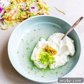 Buttermilk Fried Chicken Sandwich 9 greek yogurt, lime zest, white vinegar, and dijon mustard in a light blue bowl with a metal spoon next to coleslaw mix
