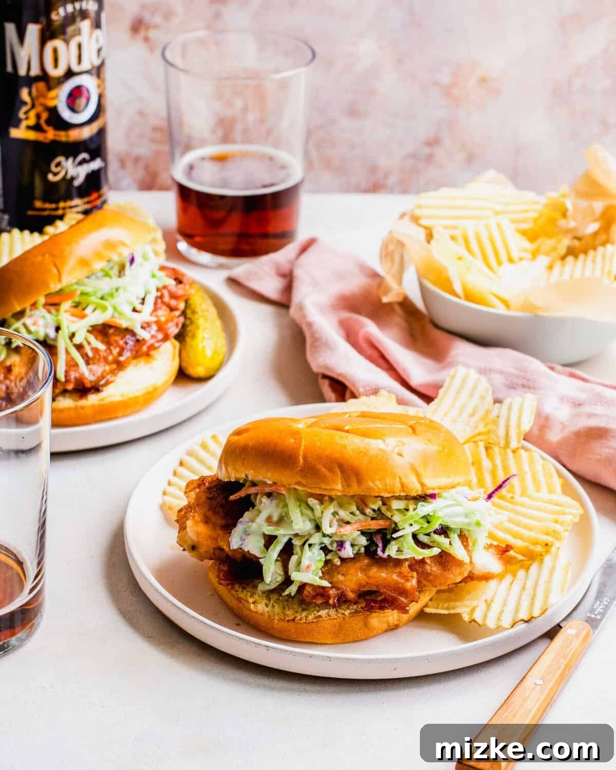 Buttermilk Fried Chicken Sandwich 4 Two plates with chicken sandwiches are placed next to a cup of beer and extra potato chips.