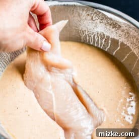 Buttermilk Fried Chicken Sandwich 7 raw chicken breast being dipped into batter in a metal bowl
