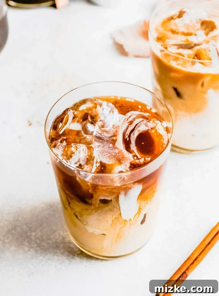 Skip the line and make an Iced Brown Sugar Oatmilk Shaken Espresso at home! This easy Starbucks copycat recipe is plant-based & delicious. Close-up shot of ice cubes clinking in a clear glass, with rich, dark espresso pouring over them, creating a perfect base for an iced coffee.