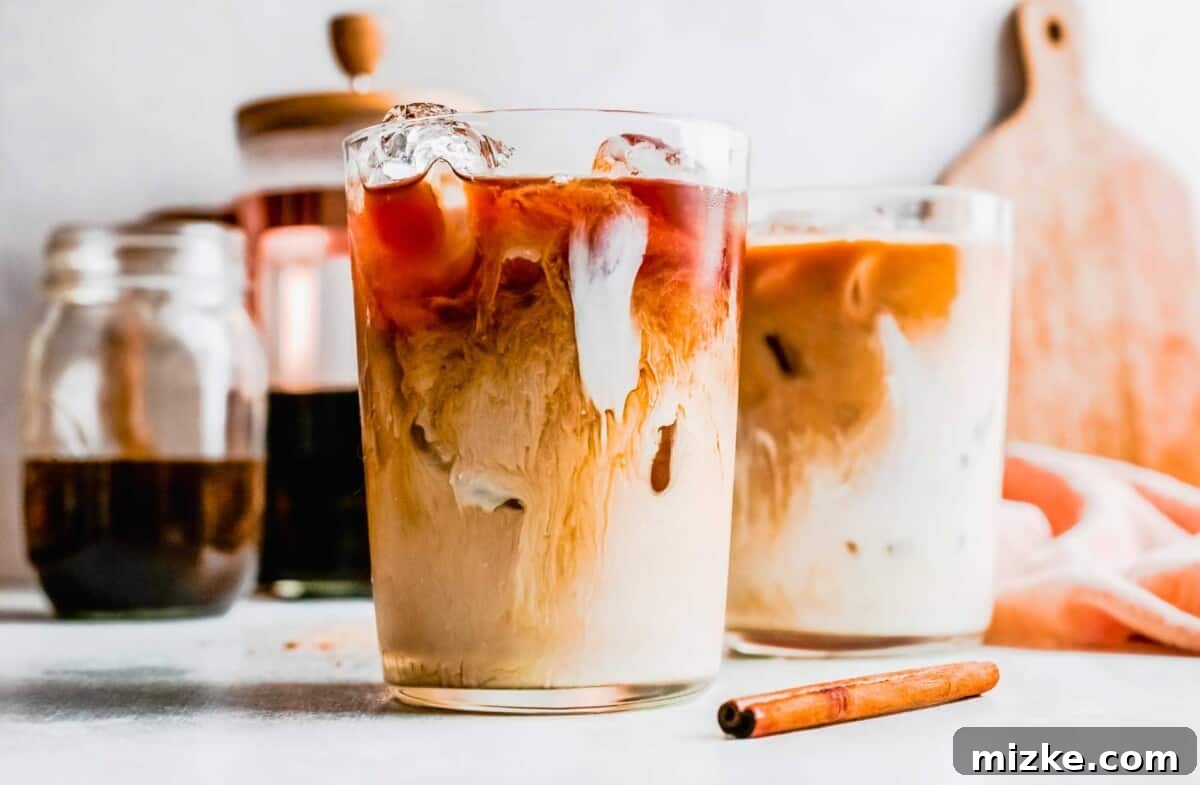 Skip the line and make an Iced Brown Sugar Oatmilk Shaken Espresso at home! This easy Starbucks copycat recipe is plant-based & delicious. Two glasses of perfectly made iced brown sugar oatmilk shaken espresso, garnished with cinnamon sticks, sitting on a pristine white surface, ready to be enjoyed.