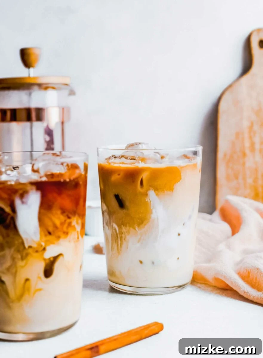 Skip the line and make an Iced Brown Sugar Oatmilk Shaken Espresso at home! This easy Starbucks copycat recipe is plant-based & delicious. Two tempting glasses of iced brown sugar oatmilk shaken espresso, accompanied by a folded tea towel on a bright white surface, inviting a refreshing coffee break.