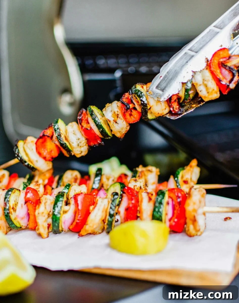 Smoky Grilled Shrimp Skewers 2 A pair of tongs is lifting a kebob from a white plate.