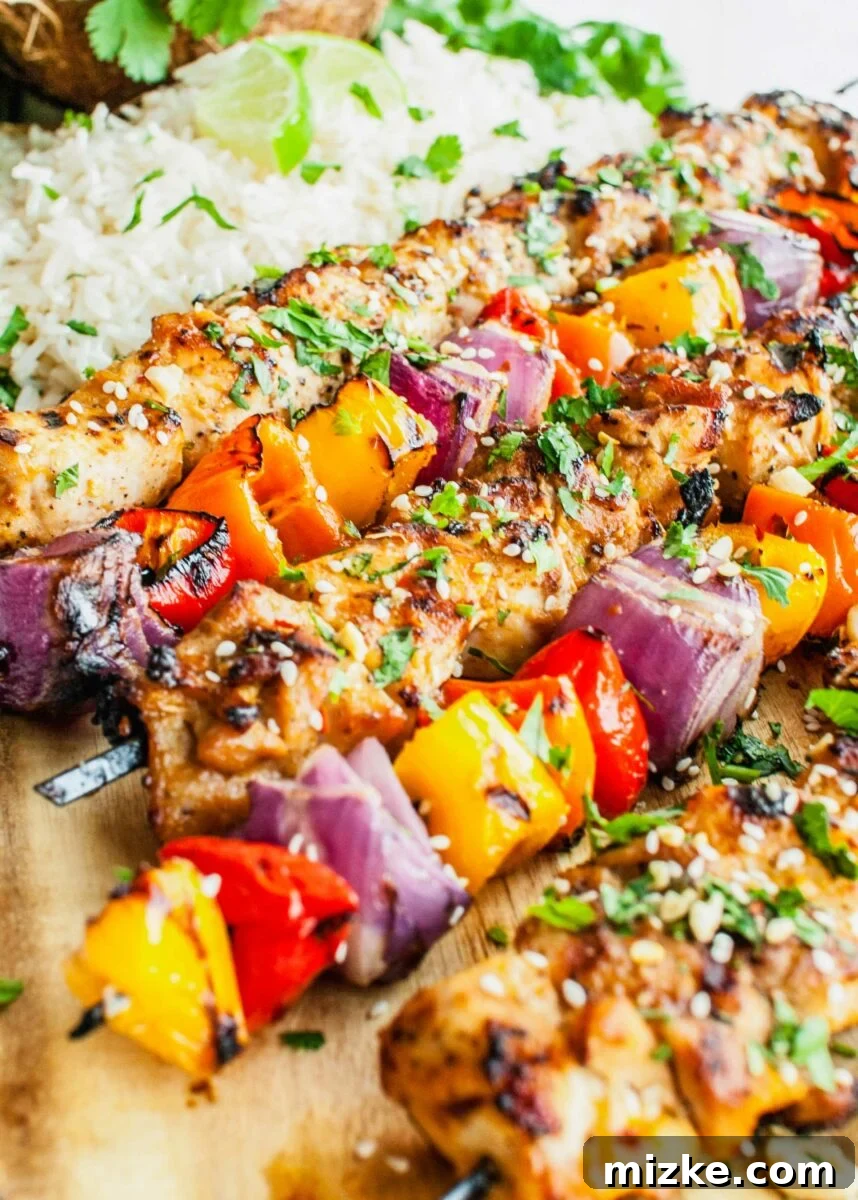 Tropical Coconut Chicken Satay 4 Close-up of sesame seeds garnishing beautifully grilled chicken skewers, served alongside a bowl of white rice.