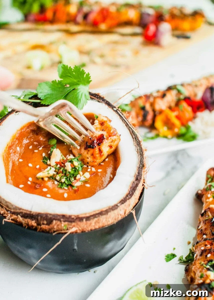 Tropical Coconut Chicken Satay 7 A piece of succulent grilled chicken is being dipped into a luscious peanut sauce, highlighting the perfect pairing.