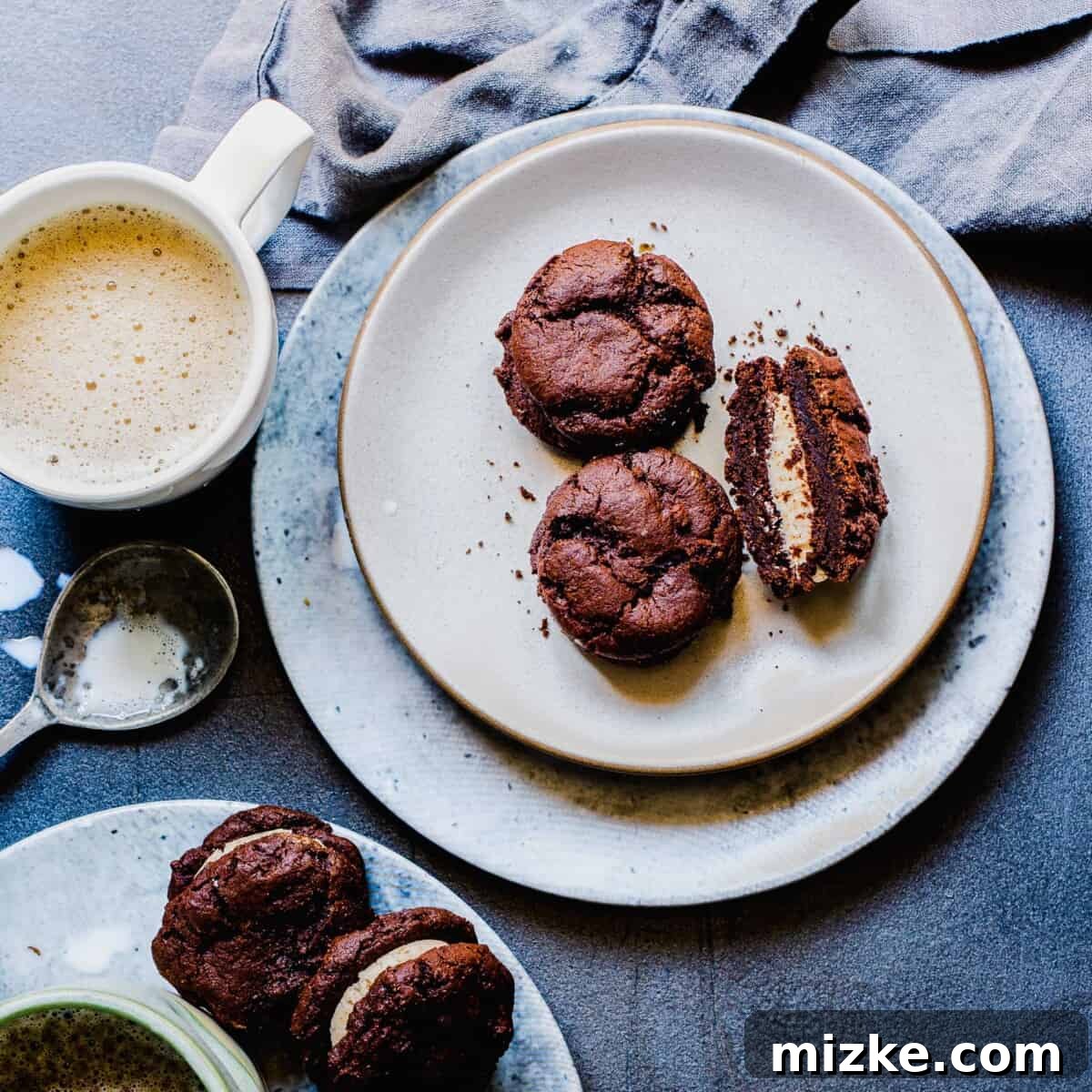 Frozen Mocha Latte Cookie Sandwiches 5 A charming mug filled with dark coffee sits next to a plate featuring three perfectly crafted mocha latte ice cream sandwiches, inviting you to enjoy this delightful pairing.