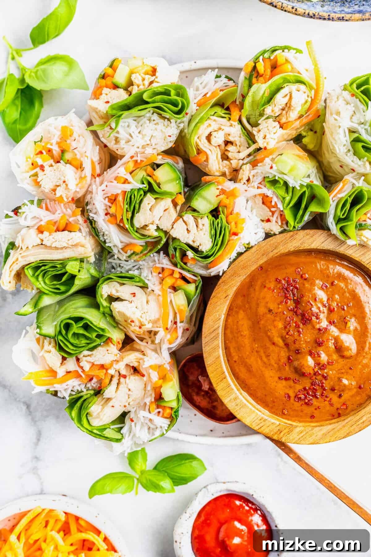Refreshing Chicken & Veggie Rolls 2 Freshly halved chicken summer rolls arranged beside a wooden bowl filled with rich satay dipping sauce.