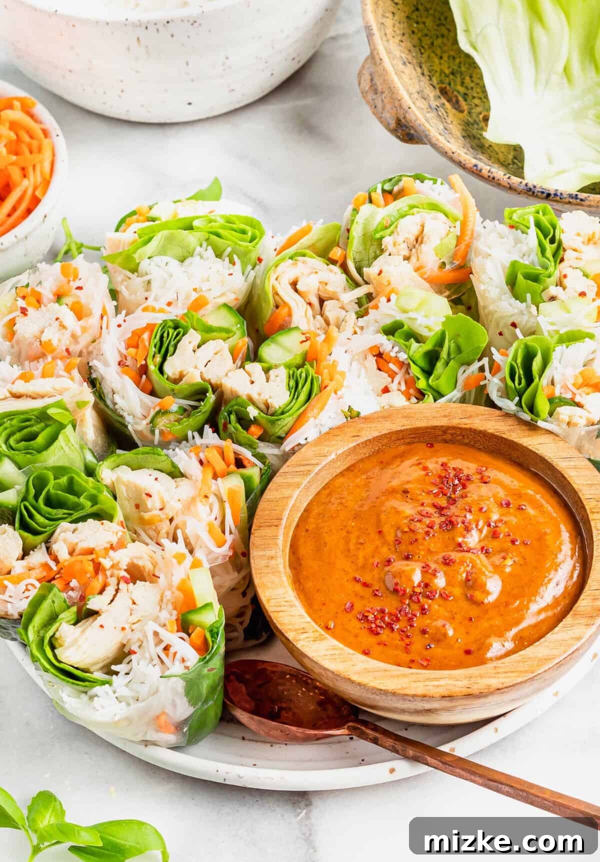 Refreshing Chicken & Veggie Rolls 3 A beautifully presented bowl of creamy satay sauce, ready for dipping, placed alongside a stack of freshly prepared chicken summer rolls.
