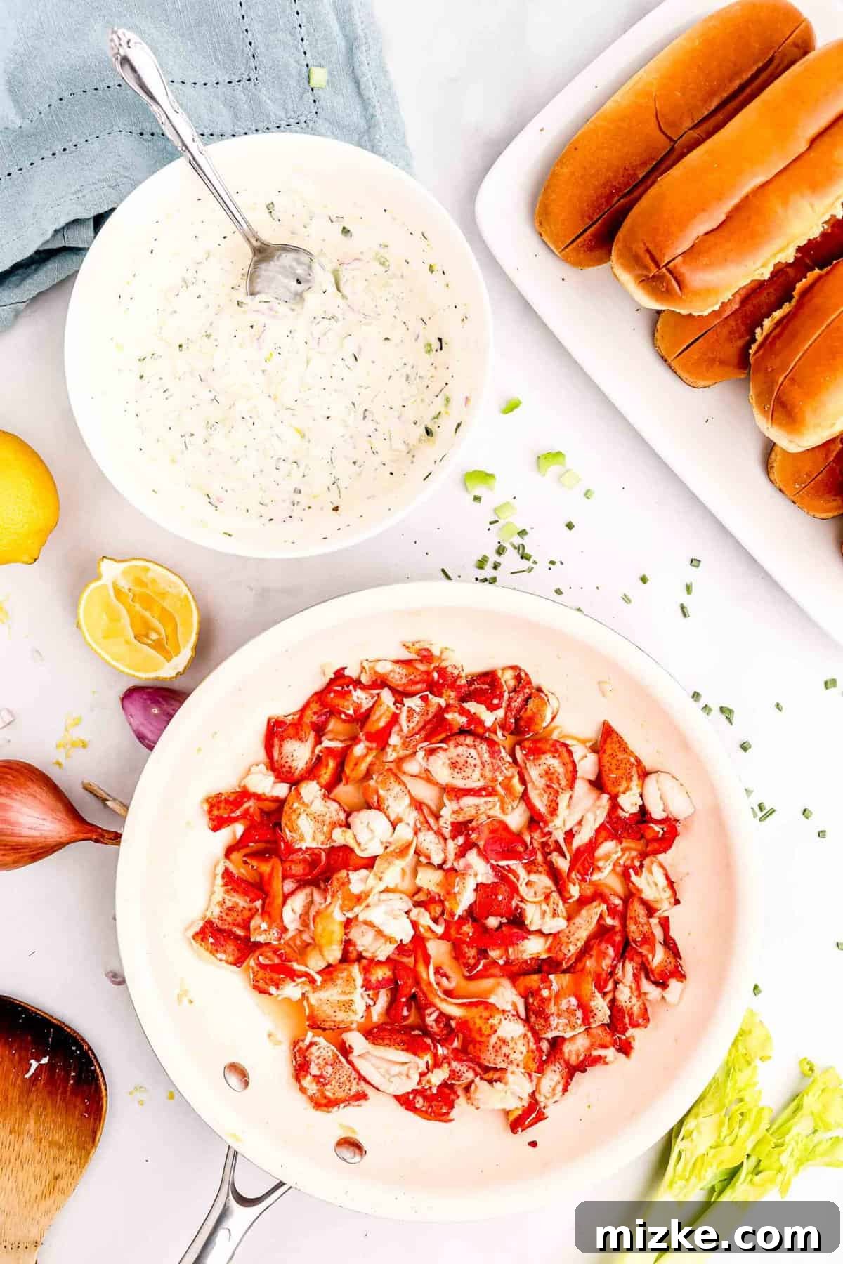 Heavenly Lobster Rolls 5 Chunks of cooked lobster meat in a skillet with melted butter, next to a bowl of creamy mayonnaise mixture and split-top brioche buns.
