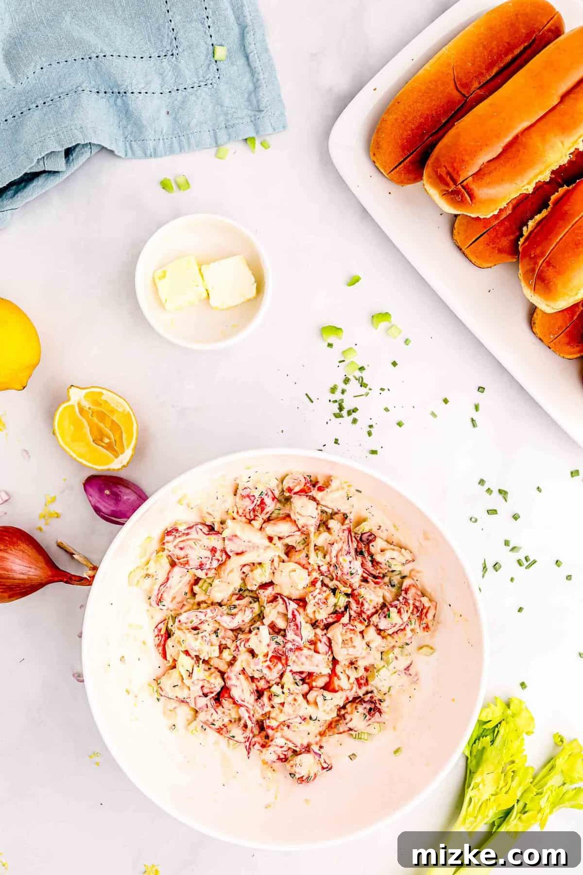 Heavenly Lobster Rolls 6 The mayonnaise mixture gently combined with the lobster meat in a white bowl, with two pads of butter and brioche buns nearby.