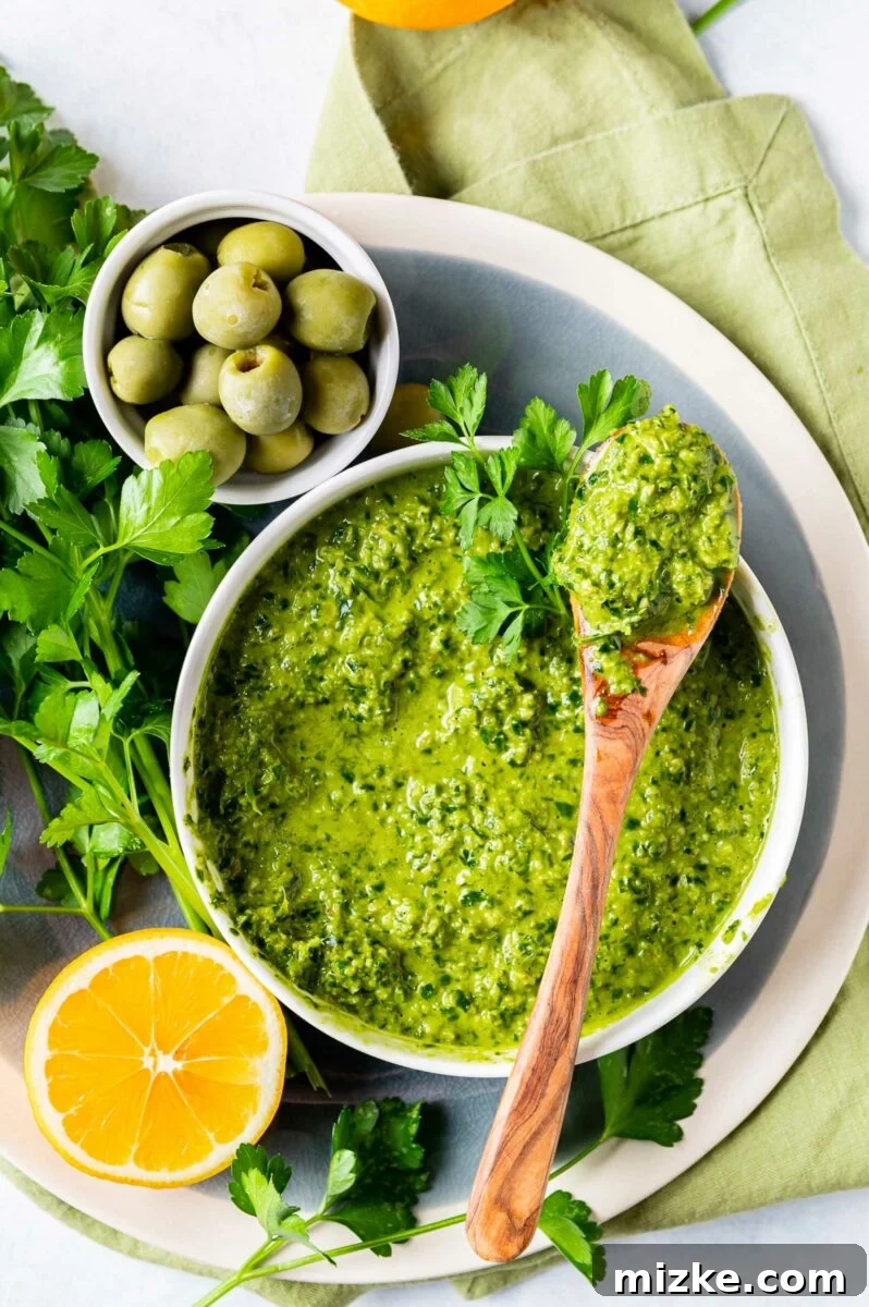 Vibrant Meyer Lemon Green Olive Gremolata 5 Gremolata is in a bowl next to lemons, herbs, and a wooden spoon.