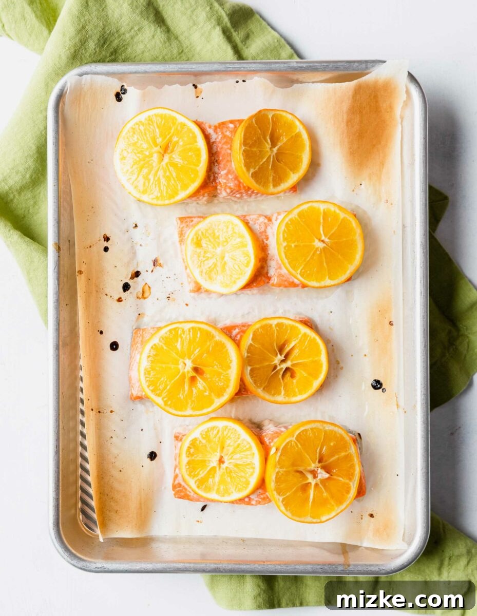 Zesty Green Olive Gremolata Roasted Salmon 6 Four salmon fillets are on a prepared baking sheet, each garnished with two lemon slices.